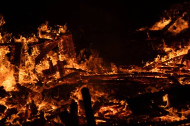 Ahşap kütükleri yutan yoğun bir ateşin yakın plan görüntüsü. Parlak alevler ve parlayan közler dramatik ve güçlü bir görüntü yaratır, ateşin ham enerjisini ve yıkıcı gücünü yakalar..