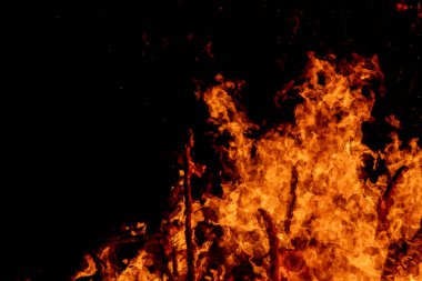 Şiddetli bir ateşin dramatik bir görüntüsü karanlık gece gökyüzüne karşı yoğun bir şekilde yanıyor. Parlak turuncu ve sarı alevler alevlerin ham enerjisini ve yıkıcı gücünü vurgular. Boşluğu kopyala.