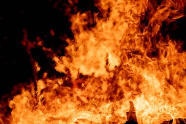 Şiddetli bir ateşin dramatik bir görüntüsü karanlık gece gökyüzüne karşı yoğun bir şekilde yanıyor. Parlak turuncu ve sarı alevler alevlerin ham enerjisini ve yıkıcı gücünü vurgular. Boşluğu kopyala.