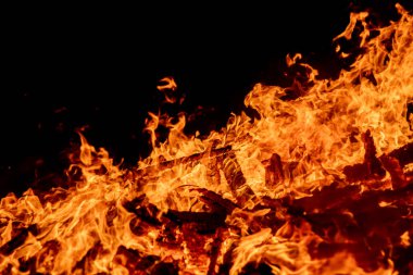 Şiddetli bir ateşin dramatik bir görüntüsü karanlık gece gökyüzüne karşı yoğun bir şekilde yanıyor. Parlak turuncu ve sarı alevler alevlerin ham enerjisini ve yıkıcı gücünü vurgular. Boşluğu kopyala.