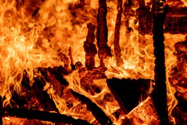 Şiddetli bir ateşin dramatik bir görüntüsü karanlık gece gökyüzüne karşı yoğun bir şekilde yanıyor. Parlak turuncu ve sarı alevler alevlerin ham enerjisini ve yıkıcı gücünü vurgular. Boşluğu kopyala.