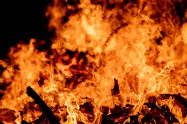 Şiddetli bir ateşin dramatik bir görüntüsü karanlık gece gökyüzüne karşı yoğun bir şekilde yanıyor. Parlak turuncu ve sarı alevler alevlerin ham enerjisini ve yıkıcı gücünü vurgular. Boşluğu kopyala.