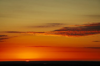 Orman ufkunun üzerinde parlak bir günbatımı, güneş gökyüzü ve manzara boyunca sıcak, altın bir parıltı yayıyor. Canlı turuncu ve sarı renkler çarpıcı ve sakin bir sahne yaratır. Boşluğu kopyala.