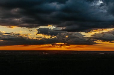 Uçsuz bucaksız orman manzarası üzerinde nefes kesici bir gün doğumu. Canlı turuncu ve sarı renkler karanlık gökyüzüne karışıyor. Dramatik bulutlar manzaraya derinlik katar. Boşluğu kopyala.
