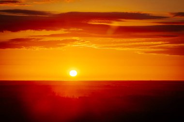 Uçsuz bucaksız orman manzarası üzerinde nefes kesici bir gün doğumu. Canlı turuncu ve sarı renkler karanlık gökyüzüne karışıyor. Dramatik bulutlar manzaraya derinlik katar. Boşluğu kopyala.