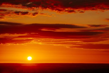 Uçsuz bucaksız orman manzarası üzerinde nefes kesici bir gün doğumu. Canlı turuncu ve sarı renkler karanlık gökyüzüne karışıyor. Dramatik bulutlar manzaraya derinlik katar. Boşluğu kopyala.