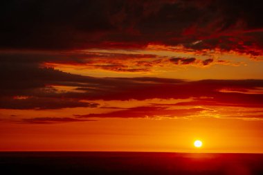 Uçsuz bucaksız orman manzarası üzerinde nefes kesici bir gün doğumu. Canlı turuncu ve sarı renkler karanlık gökyüzüne karışıyor. Dramatik bulutlar manzaraya derinlik katar. Boşluğu kopyala.