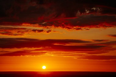 Uçsuz bucaksız orman manzarası üzerinde nefes kesici bir gün doğumu. Canlı turuncu ve sarı renkler karanlık gökyüzüne karışıyor. Dramatik bulutlar manzaraya derinlik katar. Boşluğu kopyala.