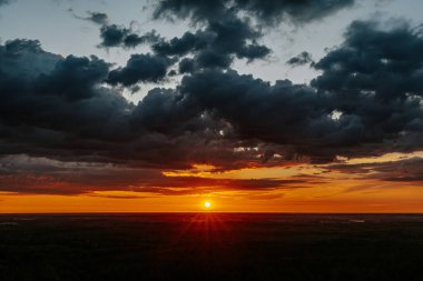 Uçsuz bucaksız orman manzarası üzerinde nefes kesici bir gün doğumu. Canlı turuncu ve sarı renkler karanlık gökyüzüne karışıyor. Dramatik bulutlar manzaraya derinlik katar. Boşluğu kopyala.