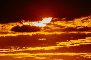 Canlı turuncu gökyüzü ile yoğun günbatımının yakın görüntüsü. Güneş belirgin bir şekilde parıldıyor ve bulutları aydınlatıyor..