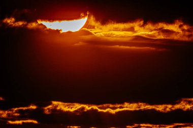 Canlı turuncu gökyüzü ile yoğun günbatımının yakın görüntüsü. Güneş belirgin bir şekilde parıldıyor ve bulutları aydınlatıyor..