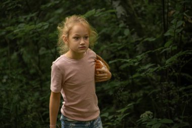 Pembe tişört giyen genç bir kız bir oyuncağı tutarak yemyeşil bir ormanı keşfediyor. Yeşillik boyunca yol alırken ifadesi bir merak ve odaklanma ifadesi..