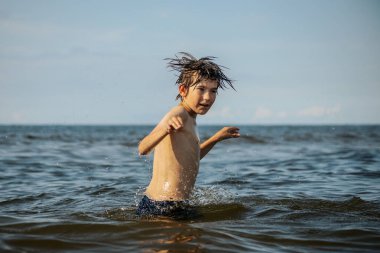 Güneşli bir günde okyanusta oynamanın heyecanını yakalayan, kolları havada suya neşeyle sıçrayan bir çocuk. Sahne, çocukluk ve yaz eğlencesinin tasasız ruhunu simgeliyor.