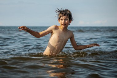 Güneşli bir günde okyanusta oynamanın heyecanını yakalayan, kolları havada suya neşeyle sıçrayan bir çocuk. Sahne, çocukluk ve yaz eğlencesinin tasasız ruhunu simgeliyor.