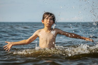 Güneşli bir günde okyanusta oynamanın heyecanını yakalayan, kolları havada suya neşeyle sıçrayan bir çocuk. Sahne, çocukluk ve yaz eğlencesinin tasasız ruhunu simgeliyor.