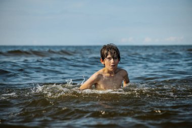 Güneşli bir günde okyanusta oynamanın heyecanını yakalayan, kolları havada suya neşeyle sıçrayan bir çocuk. Sahne, çocukluk ve yaz eğlencesinin tasasız ruhunu simgeliyor.