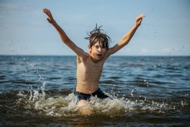Güneşli bir günde okyanusta oynamanın heyecanını yakalayan, kolları havada suya neşeyle sıçrayan bir çocuk. Sahne, çocukluk ve yaz eğlencesinin tasasız ruhunu simgeliyor.