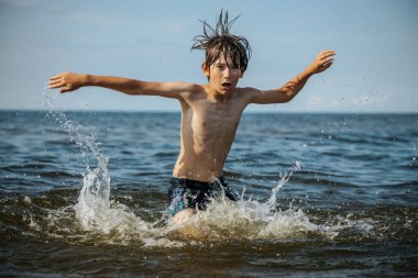Güneşli bir günde okyanusta oynamanın heyecanını yakalayan, kolları havada suya neşeyle sıçrayan bir çocuk. Sahne, çocukluk ve yaz eğlencesinin tasasız ruhunu simgeliyor.