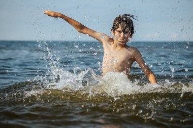Güneşli bir günde okyanusta oynamanın heyecanını yakalayan, kolları havada suya neşeyle sıçrayan bir çocuk. Sahne, çocukluk ve yaz eğlencesinin tasasız ruhunu simgeliyor.