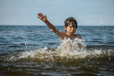 Güneşli bir günde okyanusta oynamanın heyecanını yakalayan, kolları havada suya neşeyle sıçrayan bir çocuk. Sahne, çocukluk ve yaz eğlencesinin tasasız ruhunu simgeliyor.