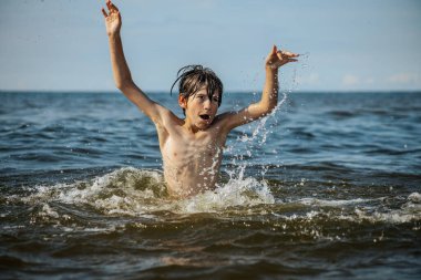 Güneşli bir günde okyanusta oynamanın heyecanını yakalayan, kolları havada suya neşeyle sıçrayan bir çocuk. Sahne, çocukluk ve yaz eğlencesinin tasasız ruhunu simgeliyor.