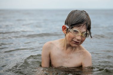 Gözlük takan bir çocuk neşeli bir ifadeyle suyun içinde duruyor, saçından damlayan su damlacıklarıyla. Sahne, bir yaz günü yüzmenin eğlencesini ve heyecanını yakalar..