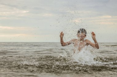 Gözlük takan bir çocuk sevinçle suya su sıçratır, heyecanla kollarını kaldırır. Sahne, çocukluk ve yaz eğlencesinin kaygısız neşesini yakalar.