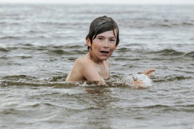 Suyun içinde çırpınan ve bağıran genç bir çocuk çevresindeki sıçramalarla ve arka planda geniş bir su birikintisiyle acı çekiyor gibi görünüyor. Sahne, aciliyet ve endişe hissi uyandırıyor.