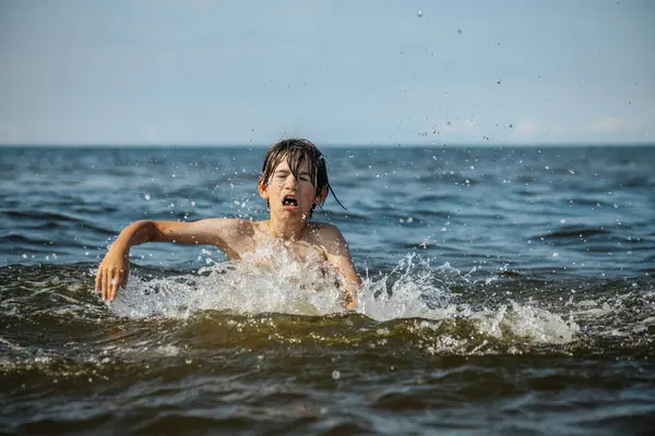 Güneşli bir günde okyanusta oynamanın heyecanını yakalayan, kolları havada suya neşeyle sıçrayan bir çocuk. Sahne, çocukluk ve yaz eğlencesinin tasasız ruhunu simgeliyor.