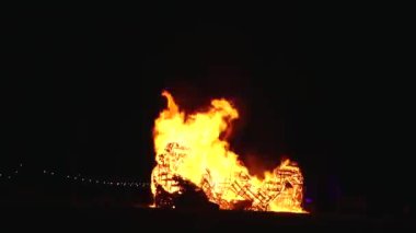 Şiddetli bir ateşin dramatik bir görüntüsü karanlık gece gökyüzüne karşı yoğun bir şekilde yanıyor. Parlak turuncu ve sarı alevler alevlerin ham enerjisini ve yıkıcı gücünü vurgular..