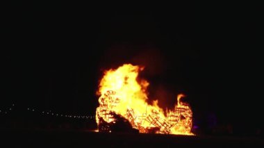 Şiddetli bir ateşin dramatik bir görüntüsü karanlık gece gökyüzüne karşı yoğun bir şekilde yanıyor. Parlak turuncu ve sarı alevler alevlerin ham enerjisini ve yıkıcı gücünü vurgular..