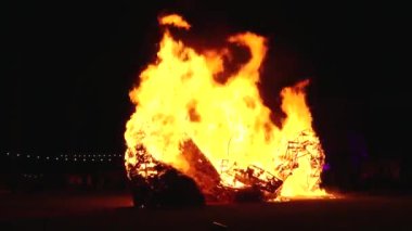 Şiddetli bir ateşin dramatik bir görüntüsü karanlık gece gökyüzüne karşı yoğun bir şekilde yanıyor. Parlak turuncu ve sarı alevler alevlerin ham enerjisini ve yıkıcı gücünü vurgular..