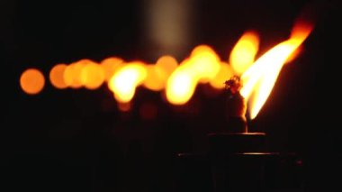 Bir sıra yanan meşalenin yakın çekimi, alevleri gecenin karanlığında sıcacık parlıyordu. Ön plandaki meşale keskin bir odak noktasındayken, diğerleri arka planda bulanıklaşarak bir huzur yaratıyor.