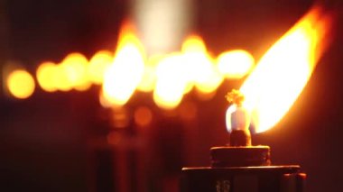 Bir sıra yanan meşalenin yakın çekimi, alevleri gecenin karanlığında sıcacık parlıyordu. Ön plandaki meşale keskin bir odak noktasındayken, diğerleri arka planda bulanıklaşarak bir huzur yaratıyor.