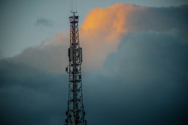 Gökyüzünü aydınlatan güneş ışığının bir ipucuyla bir iletişim kulesi bulutların arkasında dimdik ayakta duruyor. Metal yapı, serin ayarlarda belirgin olup, yeterli kopya alanı sağlar.