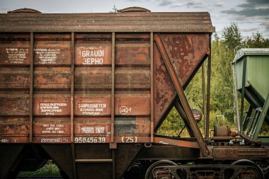 Paralel tren raylarında, eskimiş kahverengi ve yeşil konteynırlar da dahil olmak üzere uzun bir yük vagonu kuyruğu bulunuyor. Sahne sanayiyi yakalar.