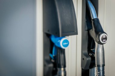 Benzin istasyonundaki yakıt hortumlarının yakın plan görüntüsü, 95E, 98E ve DD Diesel seçenekleri sunuyor. Hortumlar düzgünce tutucularına yerleştiriliyor ve istasyonların yakıt ihtiyacını karşılıyorlar..