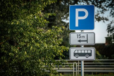 15 metrelik bir alanı gösteren bir otobüs parkı tabelası, yemyeşil ağaçlarla çevrili. Mavi ve beyaz tabela açıkça görülüyor, otobüs şoförlerini kırsal kesimdeki park yerine yönlendiriyor.