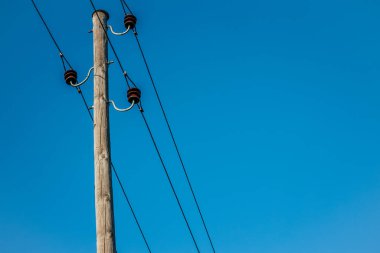 Açık mavi gökyüzüne bağlı elektrik kabloları ve yalıtımlı ahşap bir elektrik direği. Minimalist kompozisyon, geniş kopya alanı ile kutbu ve yapısını vurgular..