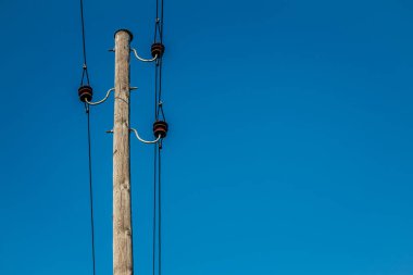 Açık mavi gökyüzüne bağlı elektrik kabloları ve yalıtımlı ahşap bir elektrik direği. Minimalist kompozisyon, geniş kopya alanı ile kutbu ve yapısını vurgular..