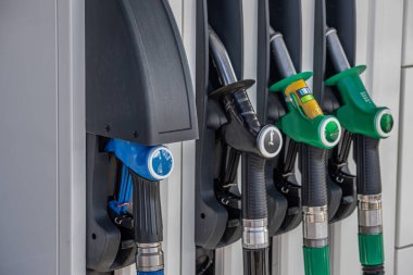 Benzin istasyonundaki yakıt hortumlarının yakın plan görüntüsü, 95E, 98E ve DD Diesel seçenekleri sunuyor. Hortumlar düzgünce tutucularına yerleştiriliyor ve istasyonların yakıt ihtiyacını karşılıyorlar..