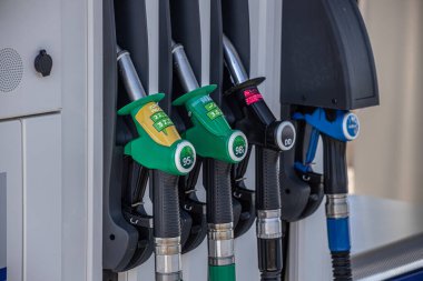 Benzin istasyonundaki yakıt hortumlarının yakın plan görüntüsü, 95E, 98E ve DD Diesel seçenekleri sunuyor. Hortumlar düzgünce tutucularına yerleştiriliyor ve istasyonların yakıt ihtiyacını karşılıyorlar..