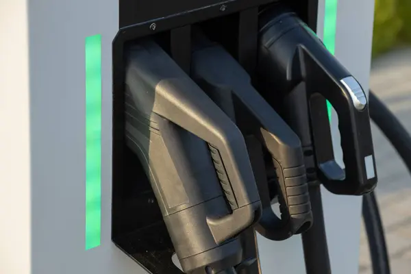 stock image A close up view of three different electric vehicle charging connectors at a charging station, labeled with their respective power outputs. An emergency stop button is visible on the right