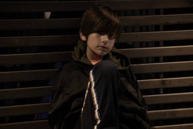 Koyu renk ceketli genç bir çocuk geceleri bankta tek başına oturur, başı eğik, üzüntüsünü ya da içyüzünü aktarır. Loş ışıklandırma ve endüstriyel çevre kasvetli atmosfere ekliyor.