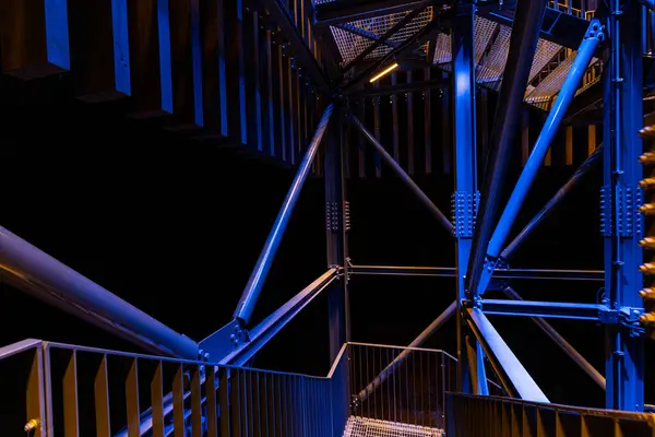 stock image A close-up, abstract view of metal beams and structures illuminated with blue and yellow lights. The geometric lines and contrasting colors create a modern, industrial aesthetic.