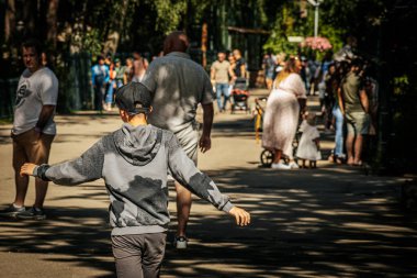 Güneşli bir günde insanların ağaçlarla kaplı bir patika boyunca yürüdüğü şehir parkındaki canlı bir sahne. Yürüyüş yolu yeşillik ve canlı çiçek yataklarıyla çevrili.