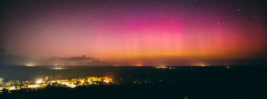 Yıldızlarla dolu nefes kesici bir gece göğü. Pembe ve mor tonlarda soluk bir aurora borealis ile aydınlanıyor. Sessiz bir kasabanın üstündeki ufku aydınlatıyor. Sahne, dingin güzelliği yakalar 