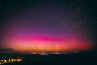 Yıldızlarla dolu nefes kesici bir gece göğü. Pembe ve mor tonlarda soluk bir aurora borealis ile aydınlanıyor. Sessiz bir kasabanın üstündeki ufku aydınlatıyor. Sahne, dingin güzelliği yakalar 