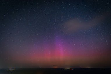 Yıldızlarla dolu nefes kesici bir gece göğü. Pembe ve mor tonlarda soluk bir aurora borealis ile aydınlanıyor. Sessiz bir kasabanın üstündeki ufku aydınlatıyor. Sahne, dingin güzelliği yakalar 