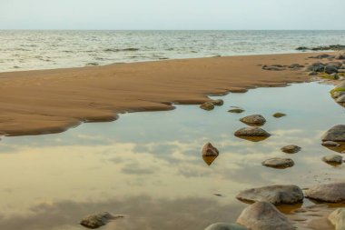 Huzurlu bir sahil, okyanusa dökülen kayalar. Durgun bir su havuzu gökyüzünü ve yumuşak akşam ışığını yansıtır. Kıyı şeridi doğal bir akış yaratarak sahnenin sakinliğini arttırır.